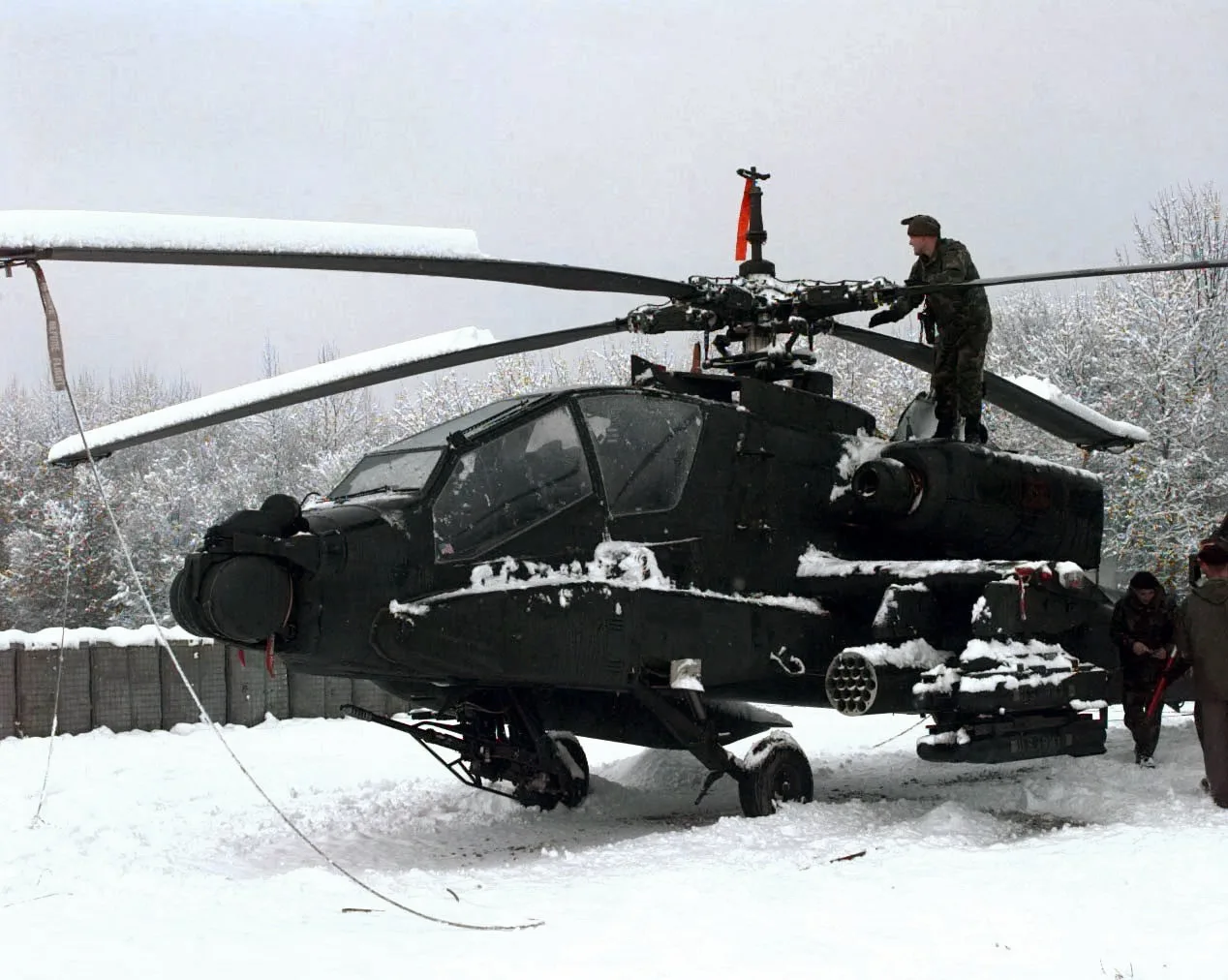 A U.S. Army soldier of the 1st Battalion 501st Aviation Brigade removes snow from the top of an AH-64A Apache attack helicopter at the Eagle Base Air Field Tuzla, Bosnia and Herzegovina, on Dec. 16, 1997. The 501st Aviation Brigade is deplo